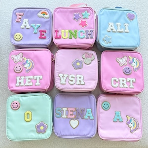 May include: Nine personalized lunch bags with different names and designs. The bags are made of a soft, pink fabric with a variety of colorful patches and embroidery. The names on the bags are: Faye, Lunch, Ali, Het, Vsr, Crt, O, Siena, and A.