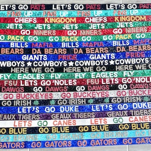May include: A collection of 18 colorful beaded straps with different team names and logos, including "Let's Go Pats", "Go Niners", "Go Dawgs", "Go Irish", "Go Gators", and "Go Bruins".