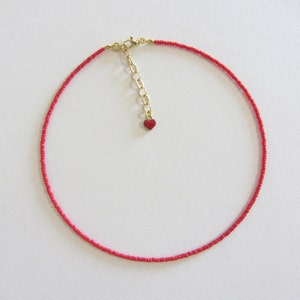 Könnte beinhalten: Eine rote Perlenkette mit einer goldenen Kette und einem kleinen roten Herz-Anhänger.