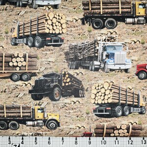 May include: A fabric pattern featuring multiple logging trucks in yellow, red, blue, and black, each carrying stacks of brown logs against a tan, textured ground. A white ruler with black markings is visible at the bottom edge of the image.