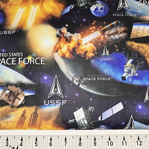 May include: Fabric with a space theme featuring rockets, satellites, planets, and the text "UNITED STATES SPACE FORCE" and "USSF" in white. The background is a dark blue with stars and orange and yellow flames.