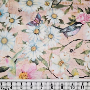 May include: Floral fabric with a vintage aesthetic. The design features white and blue daisies, pink roses, a hummingbird, a bird, and a butterfly. The background is a soft pink with subtle texturing. The fabric is measured with a cm ruler.