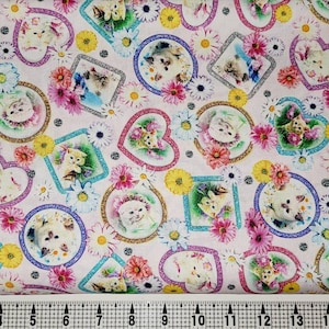 May include: Pink fabric with a repeating pattern of white kittens in colourful frames and flowers. The frames are in the shape of hearts, circles and squares.