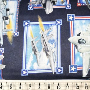 May include: A navy blue fabric with a repeating pattern of fighter jets in various poses. The jets are depicted against a backdrop of clouds and stars. The fabric features red, white, and blue accents.
