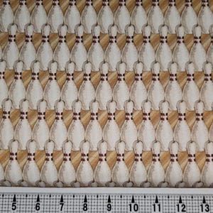 以下が含まれることがあります： 茶色と白のボーリングピンの繰り返しパターンが施された白い生地。生地はベージュの背景に、かすかなストライプ模様が施されています。