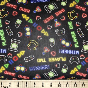 Könnte beinhalten: Schwarzer Stoff mit einem pixeligen Videospiel-Design. Das Muster umfasst Gamecontroller, Spielautomaten, Kopfhörer und die Wörter "GAME OVER", "PLAYER ONE" und "WINNER!" in verschiedenen Farben.