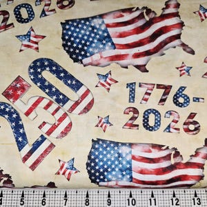 May include: Fabric with a patriotic theme featuring the American flag, stars, and the outline of the United States. The numbers "1776-2026" and "2026" are also visible. The fabric has a beige background.