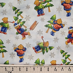 May include: Light blue fabric with a repeating pattern of cartoon bears in winter attire. The bears are wearing coats, hats, and scarves, with snowflakes and green pine trees scattered throughout the design. A ruler is at the bottom.