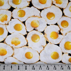 May include: A close-up of a fabric with a repeating pattern of fried eggs. The eggs are yellow and white and are arranged in a random pattern.