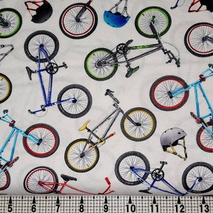 May include: White fabric with a repeating pattern of blue, red, and green BMX bikes and helmets.