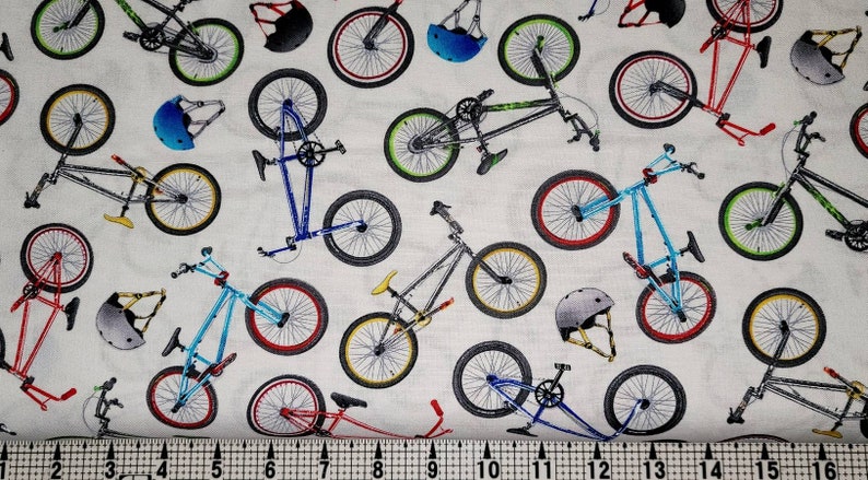 May include: White fabric with a repeating pattern of blue, red, and green BMX bikes and helmets.