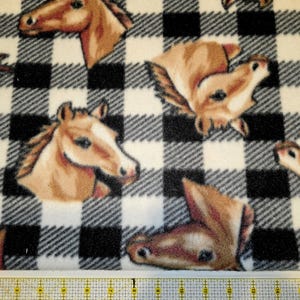 May include: A fabric with a black and white checkered pattern featuring multiple horse head illustrations in shades of brown and tan. The fabric is likely fleece or a similar soft material.