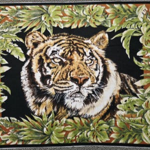 May include: A textile featuring a detailed tiger face surrounded by green and brown tropical leaves against a black background. The tiger has orange and black stripes with a white face and chest. The leaves have a detailed, realistic appearance.