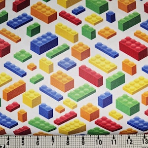 May include: Fabric with a repeating pattern of colorful toy building blocks in red, orange, yellow, green, and blue on a white background. The blocks are of various sizes and shapes, creating a playful design.