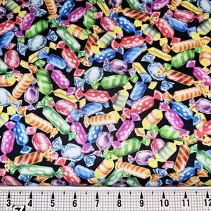Op de afbeelding: Een zwarte stof met een herhalend patroon van kleurrijke ingepakte snoepjes. De snoepjes zijn in verschillende vormen en maten, waaronder swirls, strepen en stippen.