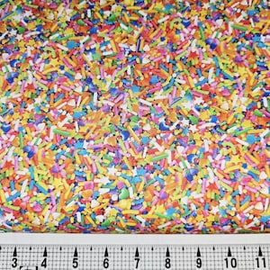May include: A vibrant fabric covered in colorful sprinkles, including blue, yellow, orange, and pink. The sprinkles are of various shapes, including stars and sticks. A ruler is at the bottom, showing measurements in inches.