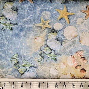 May include: Fabric with a beach theme featuring seashells, starfish, and pebbles on a blue and tan background. The design evokes a shallow ocean scene with light reflecting on the water. The fabric is suitable for various craft projects.