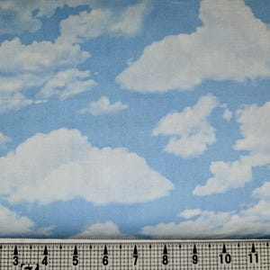 Op de afbeelding: Een blauwe stof met een witte wolkendruk. De stof wordt gemeten met een liniaal in inches.