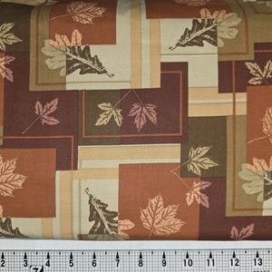 May include: Fabric with a repeating pattern of autumn leaves in shades of brown, orange, and beige. The leaves are set within a grid of squares and rectangles. The ruler at the bottom measures up to 15 inches.