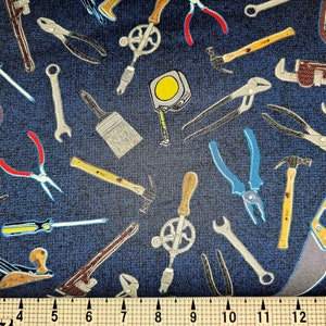 Peut inclure: Tissu bleu foncé orné d'outils à main variés. On y trouve des marteaux, des clés, des pinces, des scies et des tournevis. Les outils sont représentés en gris, jaune, marron et bleu, formant un motif dense et varié.