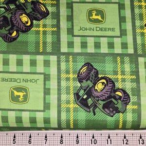 May include: Green and yellow fabric with a repeating pattern of John Deere tractors and logos. The fabric has a plaid design.