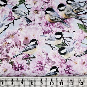 May include: A fabric with a repeating pattern of pink flowers and small birds. The birds are brown, white, and gray with black eyes. The background is a light blue.