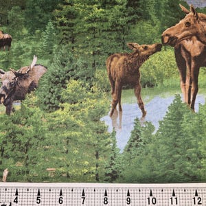 May include: A fabric with a repeating pattern of moose in a forest setting. The moose are brown and are standing in a green forest with blue water in the background.