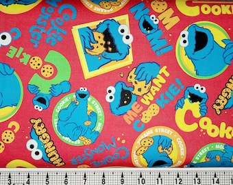 May include: Red fabric featuring the Cookie Monster from Sesame Street. The design includes the Cookie Monster character, cookies, and text such as "Cookie Monster", "Me Want Cookie!", and "Hungry".