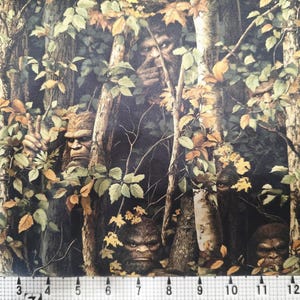 May include: A fabric design depicting a forest scene with multiple Bigfoot figures concealed within the trees and leaves. The colour scheme is dominated by greens, browns, and yellows, creating a camouflage effect. The Bigfoot figures have detailed facial features and fur.