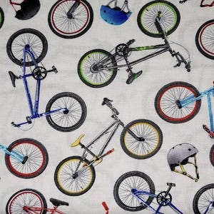 May include: A white fabric with a repeating pattern of colorful BMX bikes and helmets. The bikes are in various colors, including blue, red, green, and yellow. The helmets are in blue and red.