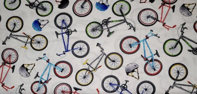 May include: A white fabric with a repeating pattern of colorful BMX bikes and helmets. The bikes are in various colors, including blue, red, green, and yellow. The helmets are in blue and red.