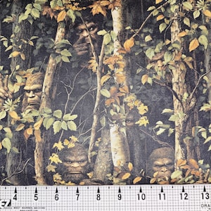 May include: A forest-themed fabric featuring multiple Bigfoot figures hidden amongst trees and leaves. The fabric's background is dark, with green, brown, and yellow hues. A ruler at the bottom displays measurements in inches.