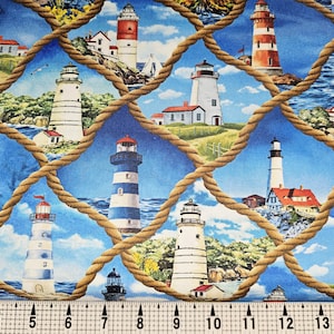 May include: Fabric with a nautical theme featuring various lighthouses in red, white, and blue against a blue sky and ocean backdrop. The design is overlaid with a rope-like grid pattern. The fabric is measured with an inch ruler.