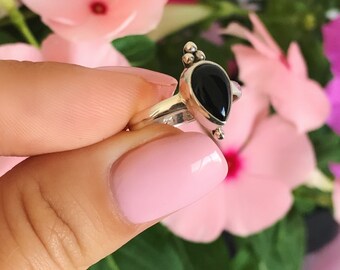 Könnte beinhalten: Ein silberner Ring mit einem schwarzen, tropfenförmigen Edelstein. Der Ring ist mit kleinen silbernen Perlen um den Edelstein besetzt.