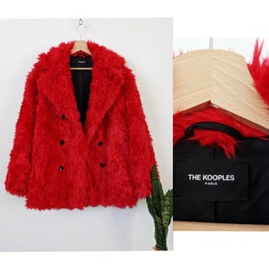 Puede incluir: Abrigo de piel sint&eacute;tica rojo con cierre de doble botonadura y botones negros. El abrigo tiene una etiqueta negra con el texto "THE KOOPLES PARIS" en el interior.