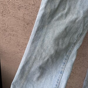 K&ouml;nnte beinhalten: Nahaufnahme von hellblauem Denim-Stoff. Der Denim hat ein strukturiertes Aussehen mit subtilen Farbvariationen und sichtbaren N&auml;hten entlang der N&auml;hte. Der Stoff ist leicht zerknittert, was darauf hindeutet, dass er getragen oder gewaschen wurde. Der Gesamteindruck ist l&auml;ssig und klassisch.