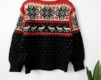 Könnte beinhalten: Ein Pullover im Vintage-Stil mit festlichem Design. Der Pullover hat einen roten Ausschnitt und eine Passe mit schwarzen Schneeflocken und Rentieren auf cremefarbenem Hintergrund. Der untere Teil ist schwarz mit weißen Punkten.