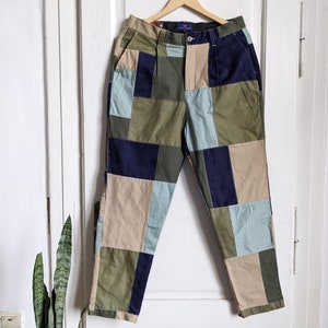 Peut inclure: Pantalon patchwork avec un mélange de carrés de tissu vert, bleu et beige. Le pantalon a une jambe droite et une coupe décontractée.