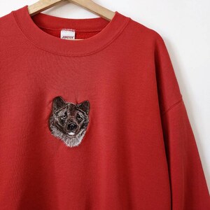 May include: Red sweatshirt with an embroidered brown dog on the front. The sweatshirt has a crew neck and the brand name "JERZEES" is visible on the tag.