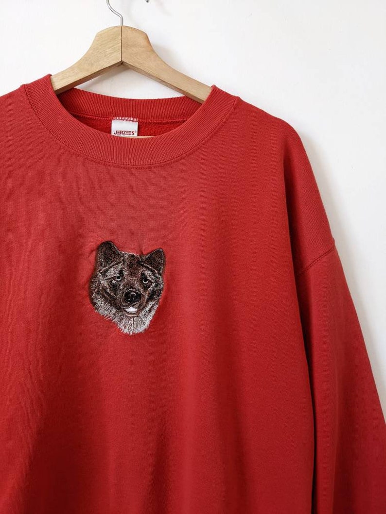 May include: Red sweatshirt with an embroidered brown dog on the front. The sweatshirt has a crew neck and the brand name "JERZEES" is visible on the tag.