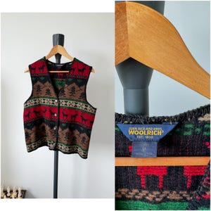 Puede incluir: Un chaleco de lana con estampado rojo, negro, verde y marrón con cierre de botón. El chaleco tiene una etiqueta que dice "John Rich and Bros. Woolrich Est. 1830."