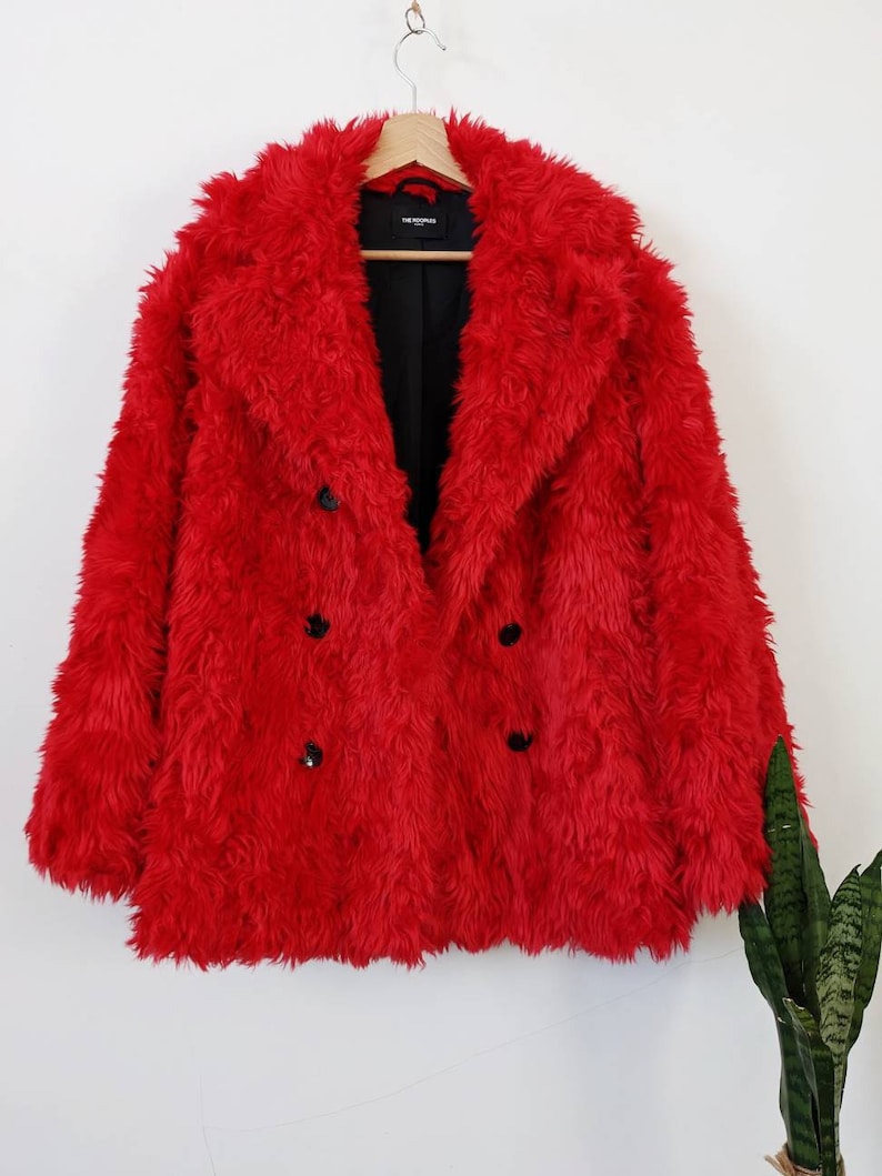 Puede incluir: Una chaqueta de piel sint&eacute;tica roja con cierre de doble botonadura y botones negros. La chaqueta est&aacute; colgada en una percha de madera.