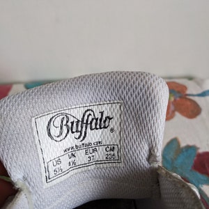 Op de afbeelding: Witte schoenzool met een zwart label waarop "Buffalo" en "www.buffalo.com" staat. Het label toont ook de schoenmaat in US, UK, EUR en CM: 5 1/2, 4 1/2, 37, 235.