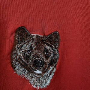 May include: Embroidered brown and white dog head on a red background.