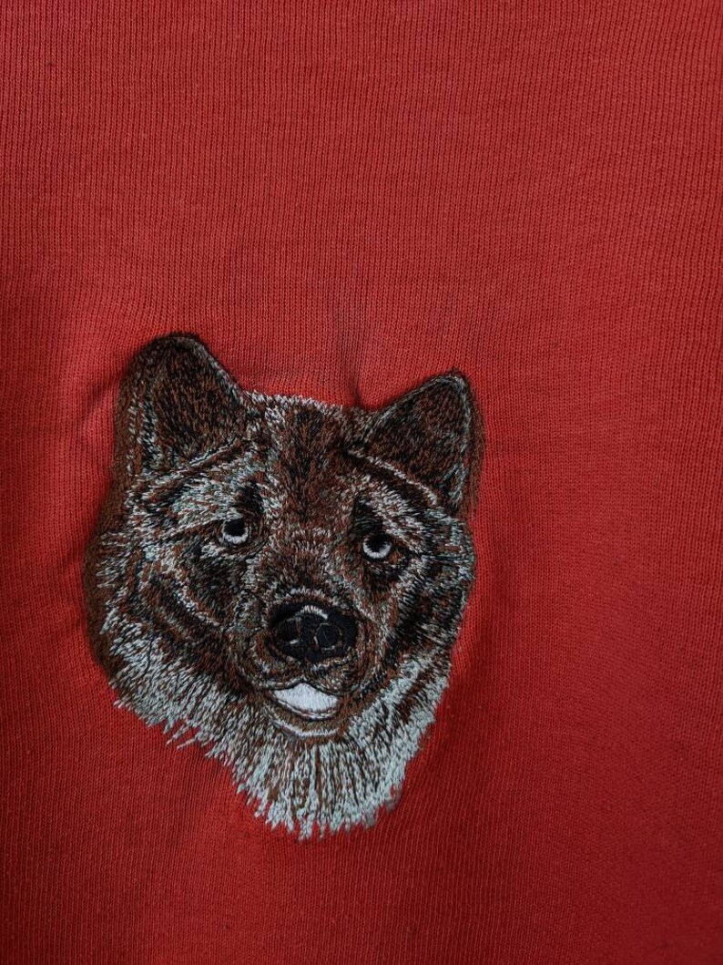 May include: Embroidered brown and white dog head on a red background.