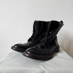 May include: A pair of black leather lace-up boots featuring a rounded toe, a visible seam running down the center of the vamp, a high-top shaft, and a dark, thick sole. The boots are constructed with black laces and have a smooth, polished finish.
