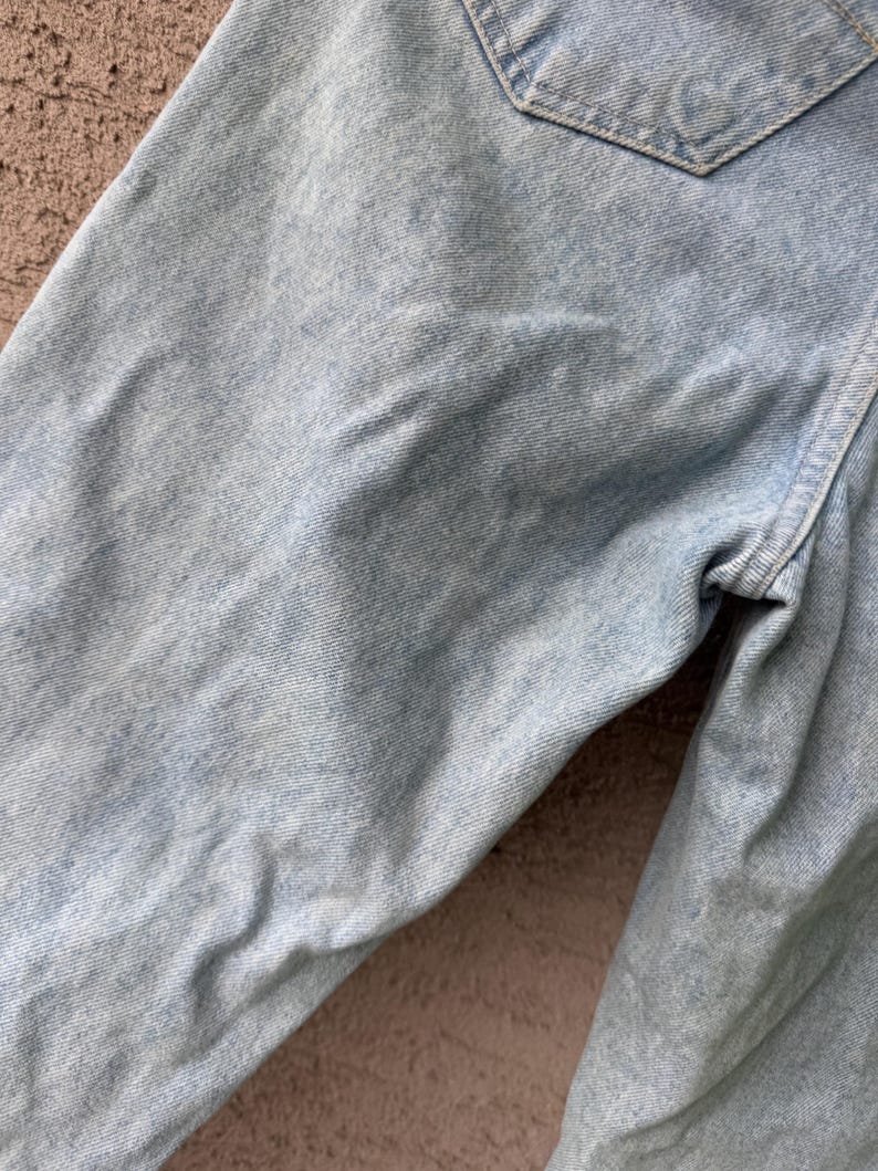 K&ouml;nnte beinhalten: Nahaufnahme einer hellblauen Jeans, die die Textur und Details des Stoffes hervorhebt. Das Bild zeigt den oberen Teil der Jeans, einschlie&szlig;lich einer Tasche und der N&auml;hte.