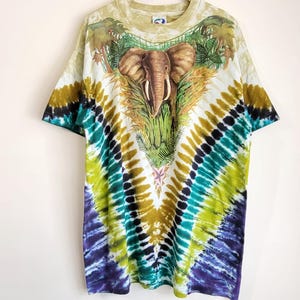 Puede incluir: Una camiseta te&ntilde;ida con un dise&ntilde;o de elefante. La camiseta tiene una base blanca con un colorido patr&oacute;n tie-dye en tonos verdes, azules y amarillos. El elefante est&aacute; representado con un dise&ntilde;o detallado, rodeado de follaje tropical.