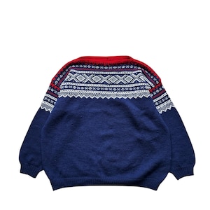 Puede incluir: Un suéter azul con cuello rojo y un patrón geométrico blanco y rojo en los hombros. El suéter tiene mangas largas y cuello redondo. La prenda de punto es de estilo clásico.