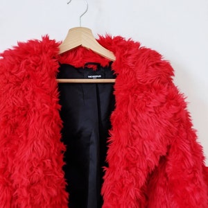 Puede incluir: Una chaqueta de piel sint&eacute;tica roja con forro negro y una etiqueta que dice "THE KOOPLES".